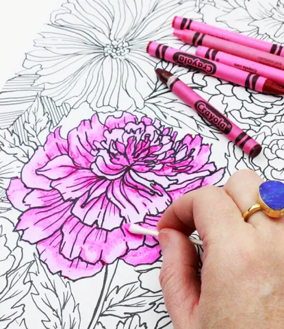 Someone using a pink crayon to color a flower