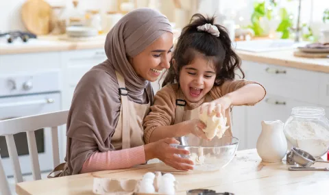 mother wearing head scarf with daughter mixing a bowl of ingredients 