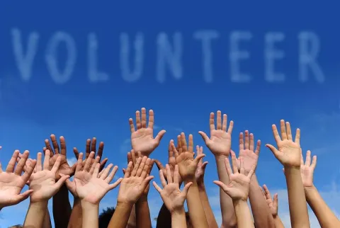 Raised hands of diverse people under the blue word volunteer