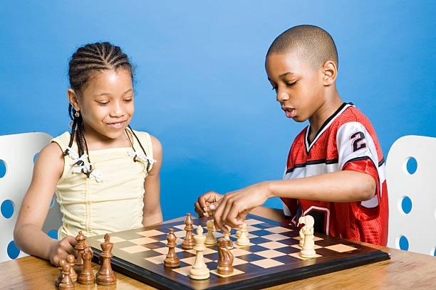 A young girl and boy playing chess against a blue background.