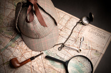 Sherlock Holmes hat, pipe, and watch resting on a map